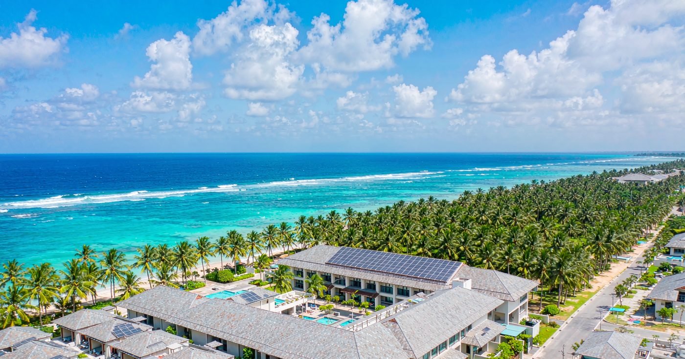 Aerial view of a beachfront resort with rooftop solar panels on the main building and villa roofs