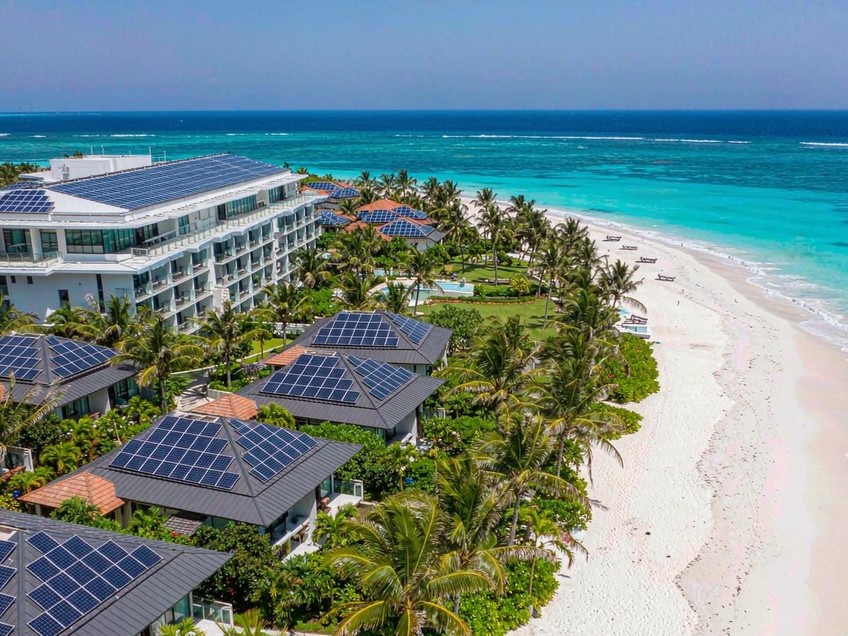Aerial view of a tropical beachfront resort with solar panels installed on the main building and villa roofs