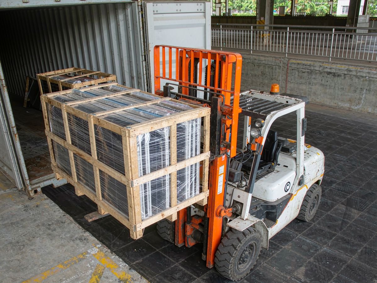 Forklift loading crated solar panels into a shipping container at a dock