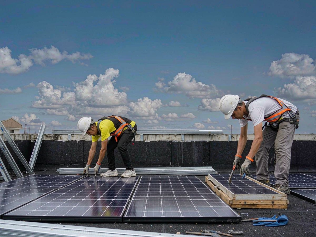 Two solar installers in safety gear mounting panels on a Philippine rooftop
